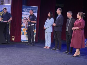 Umundurowani policjanci oraz uczestnicy na scenie. W tle banery.