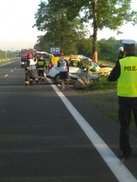 miejsce wypadku drogowego w Ochabach. W tle policjant, strażacy i uszkodzony samochód