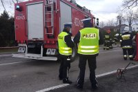 Policjanci i strażacy na miejscu zdarzenia drogowego przy uszkodzonych pojazdach wykonują czynności służbowe