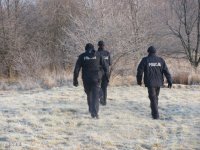 troje policjantó w trakcie patrolu- idą w kjierunku lasu w zimowej aurze