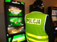 policjant w kamizelce odblaskowej z napisem  Policja stojący tyłem do fotografa, po lewej automat do gier