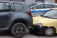 samochód fiat z prawej strony najechał na dacię z lewej strony zdjęcia. W tle policyjny radiowóz