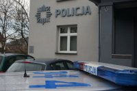 radiowóz, w tle napis policja na budynku komisariatu