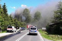 płonący budynek, dym unosi się wysoko w kierunku nieba. Widoczny radiowóz policji oraz samochód straży pożarnej