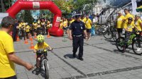 dzieci jadą na rowerze w obecności pilnującego ich policjant. Wokół wiele innych osób