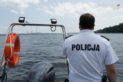 policjant na motorówce patroluje akwen wodny, napis polcja na plecach, przed policjantem woda akwenu