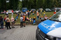 grupa dzieci na spotkaniu z policjantem, siedzą i słuchają na zewnątrz, w plenerze