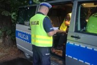 policjant stoi tyłem, przodem w kierunku radiowozu