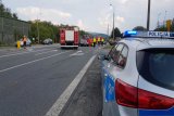 radiowóz policyjny, w tle wypadek- straż pożarna oraz policjanci wykonują czynności na miejscu zdarzenia