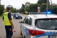 policjant stoi przy radiowozie i obserwuje ruch na drdze