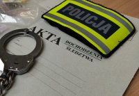 kajdanki, opaska z napisem policja leżą na tekturze z napisem akta sprawy