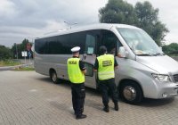 grafika- policjant i inspektor transportu drogowego stoją tyłem i patrzą na kontrolowany autobus