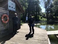 niebo, akwen wodny, pomost na wodzie- na nim stoi policjant oraz zarządzający akwenem mężczyzna