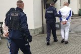 zdjęcie-policjanci prowadzą osoby zatrzymane, które mają założone kajdanki na ręce trzymane z tyłu