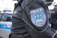 policyjna naszywka na ramieniu kurtki, w tle pojazd policji