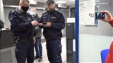 osoba trzyma w ręce telefon i nagrywa policjantów. Jeden z policjantów trzyma dowód osobisty, drugi telefon