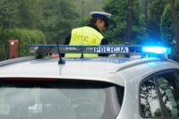 policyjny radiowóz z włączonymi niebieskimi sygnałami błyskowymi, w tle policjant ruchu drogowego