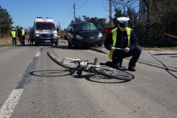 policjant w przysiadzie przy rowerze leżącym na jezdni, w tle karetka