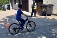 grafika-chłopiec jedzie na rowerze, w tle policjant go obserwuje