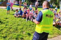 grafika-dzień, plener, policjant rozmawia z dziećmi,