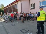 policjant rozmawia z uczniami, którzy trzymają rowery