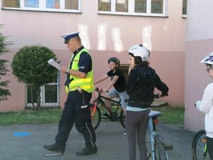 policjant w mundurze trzyma w ręku kartkę i ocenia jazdę dziecka na rowerze