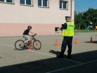 policjant w mundurze trzyma w ręku kartkę i ocenia jazdę dziecka na rowerze