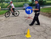 zdjęcie-dzień,policjant, dziecko na rowerze, znaki drogowe. Mundurowy egzaminuje dziecko na kartę rowerową