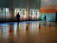 hala gimnastyczna, ułożony tor przeszkód dla rowerzystów, policjant obserwuje jak dziecko jedzie na rowerze