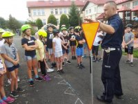 policjant rozmawia z dziećmi na zewnątrz, pokazuje znak drogowy