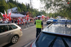 policjant stoi na jezdni i obserwuje ruch pieszych, stoi tyłem do obiektywu, przed nim przemieszczają się kibice w biało czerwonych barwach