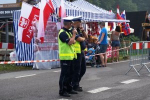 policjanci obserwują ruch na drodze, za nimi stoisko z flagami i szalikami