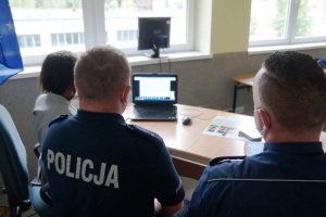 męzczyzna siedzi tyłem, napis policja na koszulce, obok kobieta, patrzą na monitor laptopa