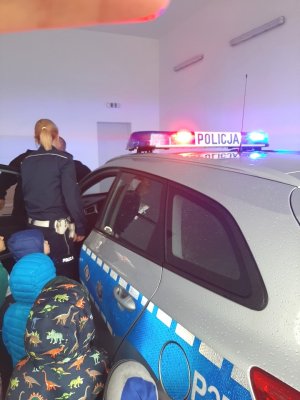 policjantka stoi przy radiowozie, dzieci się jej przyglądają