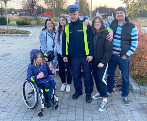 policjant oraz grupa ludzi pozuje do zdjęcia, dzień, zewnątrz budynku, parking