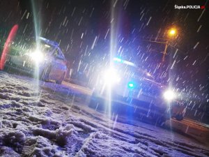 grafika-noc, policyjny radiowóz,włączone światła pojazdu opady sniegu