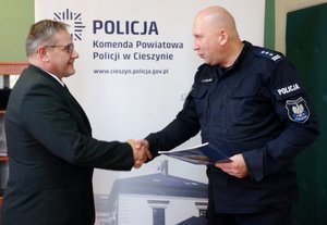 grafika-pomieszczenie, dzień,komendant ściska dłoń aspirantowi Leszkowi Krzywdzie gratulując awansu