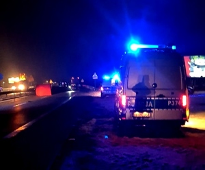 grafika-noc, droga, pojazd policji z włączonymi światłami uprzywilejowania, na jezdni widoczny czerwony parawan