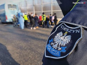 dzień, godło Polski na naszywce kurtki,napis Policja Cieszyn,  w tle autobus