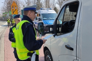 grafika,dzień ,jezdnia, policjant kontroluje busa, rozmawia z kierowcą i sprawdza przewożony ładunek