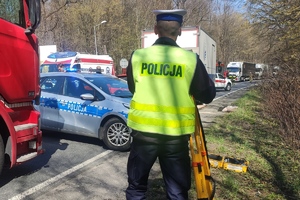 grafika-miejsce zdarzenia, dzień, pojazd ciężarowy a za nim samochód osobowy, służby ratownicze, policja, straż pożarna, pogotowie