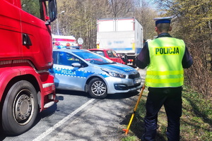 grafika-miejsce zdarzenia, dzień, pojazd ciężarowy a za nim samochód osobowy, służby ratownicze, policja, straż pożarna, pogotowie