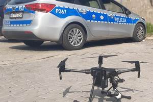 grafika-dzień, dron, w tle radiowóz policji