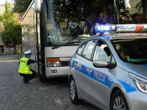 policjant w przysiadzie kontroluje opony autokaru, dzień, słonecznie, radiowóz