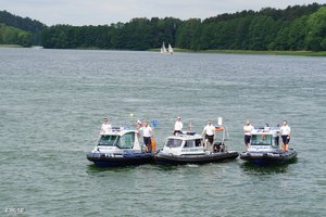 grafika, dzień, akwen wodny, policjanci na łódkach, w tle góry