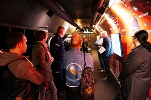 osoby zgromadzone w pociągu interaktywnym, ciemne wnętrze, słuchają przewodnika