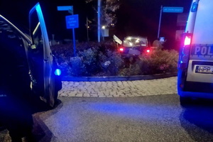 grafika-noc, samochód stoi na zieleńcu na rondzie, obok policyjny radiowóz