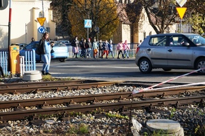 dzień, słonecznie, tory kolejowe, osoby przechodzą przez nie, samochód porusza się jezdnią