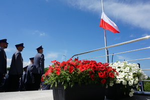 grafika-dzień, policjanci obserwują wznoszącą się na maszcie flagę Polski