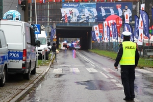 grafika-dzień, droga, policjanci na drodze i przejście dla pieszych, w tle skocznia i radiowozy oraz kibice